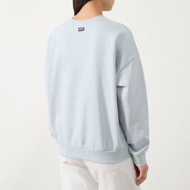 Model wearing Barbour International Pearl Blue cotton crew neck sweatshirt, shown from the back, with white trousers