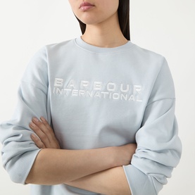 Model wearing Barbour International Pearl Blue cotton sweatshirt with embossed logo lettering across chest, arms crossed