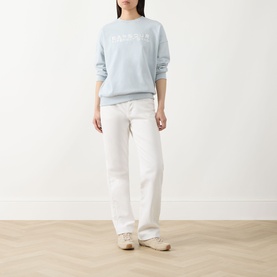 Model wearing Barbour International Pearl Blue cotton sweatshirt with logo print, styled with wide-leg white jeans and cream trainers.
