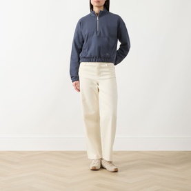 Model wearing Barbour International cropped half-zip sweat in Odyssey blue, styled with cream wide-leg trousers and white loafers.