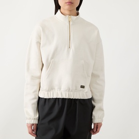 Model wearing Barbour International Light Stone cotton half-zip sweatshirt with gold zip, elasticated hem, styled with black wide-leg trousers
