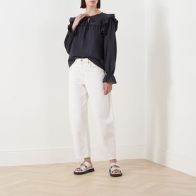 Model wearing Barbour Carleen Ruffled Blouse in Dark Navy with ruffle shoulders, styled with white cropped jeans and silver sandals.