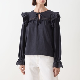 Model wearing Barbour Carleen Ruffled Blouse in Dark Navy with ruffle shoulders, flared cuffs, and keyhole neckline, styled with white trousers