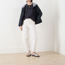 Model wearing Barbour Carleen Ruffled Blouse in Dark Navy with white straight-leg jeans, navy jacket, and silver flat sandals.