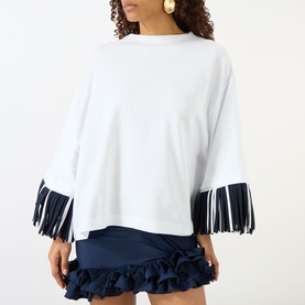 Model wearing Jacquemus white cotton T-shirt with navy fringe-trimmed sleeves, styled with a navy ruffled mini skirt.