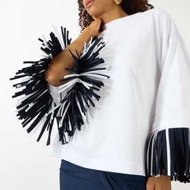 Model wearing Jacquemus white cotton T-shirt with oversized black and white fringe embellishment at chest, paired with navy trousers