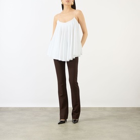 Model wearing Jacquemus white pleated cami top, styled with dark brown flared trousers and black pointed heels.