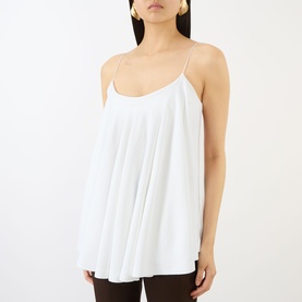 Model wearing Jacquemus white sleeveless cami top with thin straps and flared silhouette, styled with dark trousers.