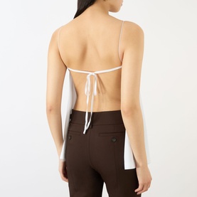 Model wearing Jacquemus white backless halterneck top with tie detail, styled with dark brown tailored trousers