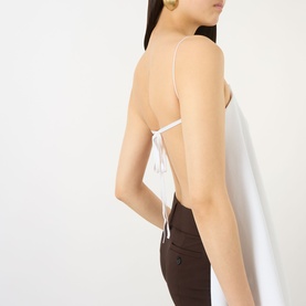 Model wearing Jacquemus white backless camisole top with thin tie-back straps, styled with dark brown trousers