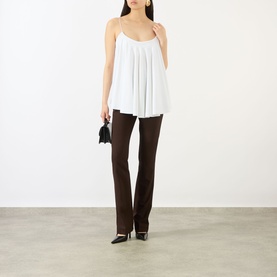 Model wearing Jacquemus white pleated cami top with spaghetti straps, styled with brown flared trousers and black pointed heels