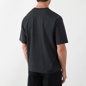 Model wearing Levis Workwear Pocket Logo T-Shirt in Jet Black, rear view showing dropped shoulders and straight hem, styled with black trousers.