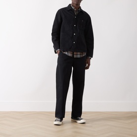 Model wearing Nudie Jeans black cotton casual jacket, styled with tartan shirt, black trousers and white-soled canvas trainers.