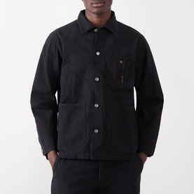 Model wearing Nudie Jeans black cotton casual jacket with chest pocket, large front pockets and grey snap buttons, styled with black trousers.