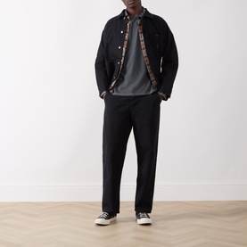 Model wearing Nudie Jeans black casual denim jacket with plaid lining, styled with grey sweatshirt, black trousers and canvas trainers.