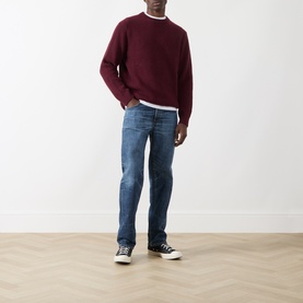 Model wearing Nudie Jeans August Rib Sweater in Burgundy ribbed wool crew neck, styled with mid-wash straight jeans and black trainers.
