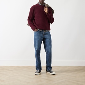 Model wearing Nudie Jeans August Rib Sweater in Burgundy ribbed wool crew neck, styled with blue jeans and navy high-top trainers.