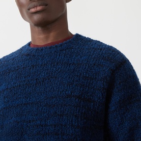 Model wearing Nudie Jeans Gurra Boucle Sweater in navy multi, textured boucle knit with crew neckline, styled with a dark red underlayer.