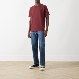 Model wearing Nudie Jeans Uno Everyday T-Shirt in Burgundy, styled with mid-wash straight jeans and black high-top trainers.
