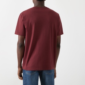 Model wearing Nudie Jeans Uno Everyday T-Shirt in Burgundy, rear view, crew neck, short sleeves, styled with blue jeans.