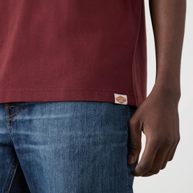 Model wearing Nudie Jeans Uno Everyday T-Shirt in Burgundy, cropped view showing Dickies label, styled with blue denim jeans.