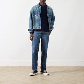 Model wearing Nudie Jeans Rad Rufus Straight-Leg Jeans in Blue Twisted Tracks, styled with a denim jacket, navy knit, and black canvas trainers.