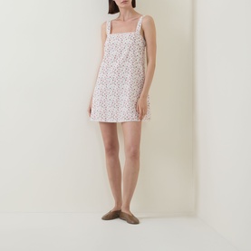 Model wearing Posse Watercolour Floral cotton mini dress with square neck and tie straps, styled with flat mule shoes.