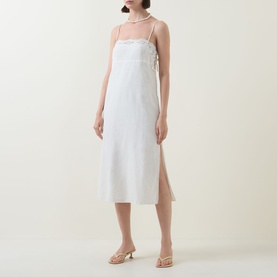 Model wearing Posse cream linen-cotton slip dress with spaghetti straps, side split and sheer neckline detail, styled with gold strappy heels