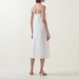 Model wearing Posse cream linen-cotton slip dress, midi length, thin straps, scallop neckline detail, shown from behind with gold mule sandals