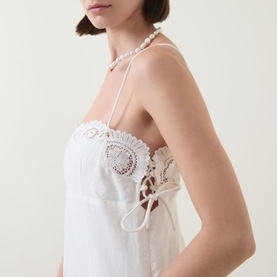 Model wearing Posse cream linen-cotton dress with crochet lace bodice detail and tie side, styled with pearl halter necklace.