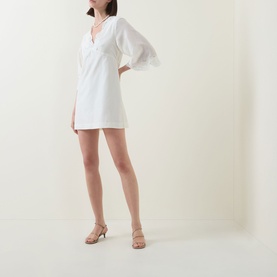 Model wearing Posse cream cotton-silk mini dress with V-neck and puffed sleeves, styled with nude strappy heeled sandals
