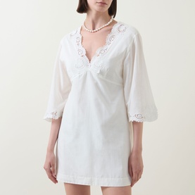 Model wearing Posse cream mini dress with V-neckline, lace trim detail, and three-quarter length sleeves, styled with pearl necklace