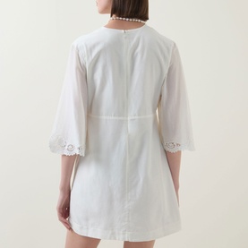 Model wearing Posse cream cotton-silk dress, rear view, with flared sleeves, broderie anglaise trim hem and cuffs, and cinched waist detail.