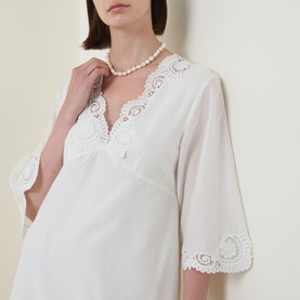 Model wearing Posse cream cotton-silk dress with V-neckline, lace trim detail and flared sleeves, styled with pearl necklace