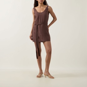 Model wearing Posse Evie Polka Dot Belted Mini Dress in Choc Vanilla, sleeveless scoop neck with draped belt detail, styled with strappy heeled mules.