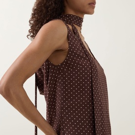 Model wearing Posse Evie Polka Dot Belted Mini Dress in Choc Vanilla, showing low-cut draped back detail and tie fastening