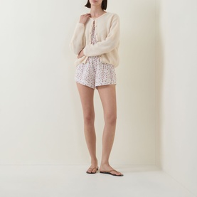 Model wearing Posse Watercolour Floral cotton shorts with cream knit sweatshirt and flat sandals.