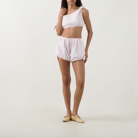 Model wearing Posse Rosie Striped Shorts in Pink Stripe, balloon-leg cotton shorts, styled with matching crop top and gold flat mules.