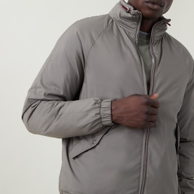 Model wearing Brunello Cucinelli olive casual jacket with zip-through collar, elasticated cuffs, and side pockets, styled over green top.