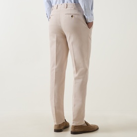 Model wearing Brunello Cucinelli sand cotton chino trousers, rear view, styled with a light blue shirt and brown suede loafers.