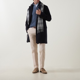 Model wearing B Cucinelli sand cotton chino trousers styled with a navy coat, blue jumper and grey check scarf.