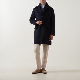 Model wearing Brunello Cucinelli navy virgin wool coat, styled with light blue shirt, beige trousers and tan suede loafers.