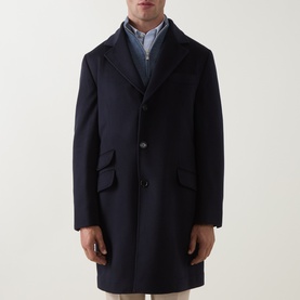 Model wearing B Cucinelli navy virgin wool coat with notched lapel, three-button front and flap pockets, styled with light blue shirt.