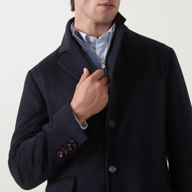 Model wearing Brunello Cucinelli navy wool coat, buttoned front, styled with striped shirt and blazer, close-up detail shot.