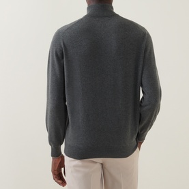 Model wearing Brunello Cucinelli dark green cashmere half-zip jumper, rear view, styled with light beige trousers.