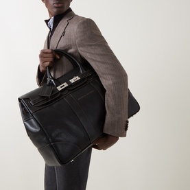 Model carrying Brunello Cucinelli Logo Grained Leather Holdall in black with silver-tone hardware and flap closure, styled with grey blazer