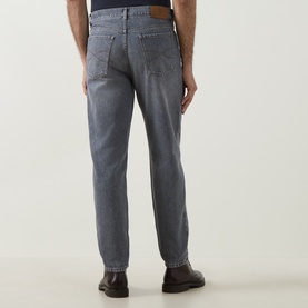Model wearing Brunello Cucinelli grey cotton jeans, rear view, styled with dark brown leather shoes.