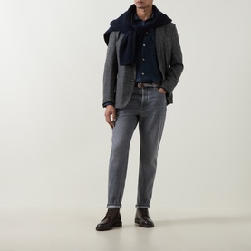 Model wearing Brunello Cucinelli grey cotton jeans, styled with a grey blazer, navy shirt and scarf, and dark brown leather boots.