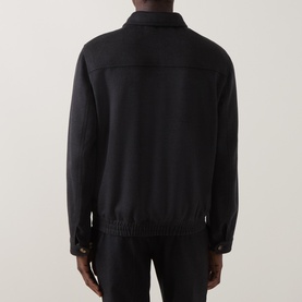 Model wearing black zip-front blouson jacket, rear view, with ribbed hem and cuffs, styled with black trousers