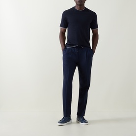 Model wearing Brunello Cucinelli BLU MARINA virgin wool trousers with drawstring waist, styled with navy T-shirt and navy trainers.
